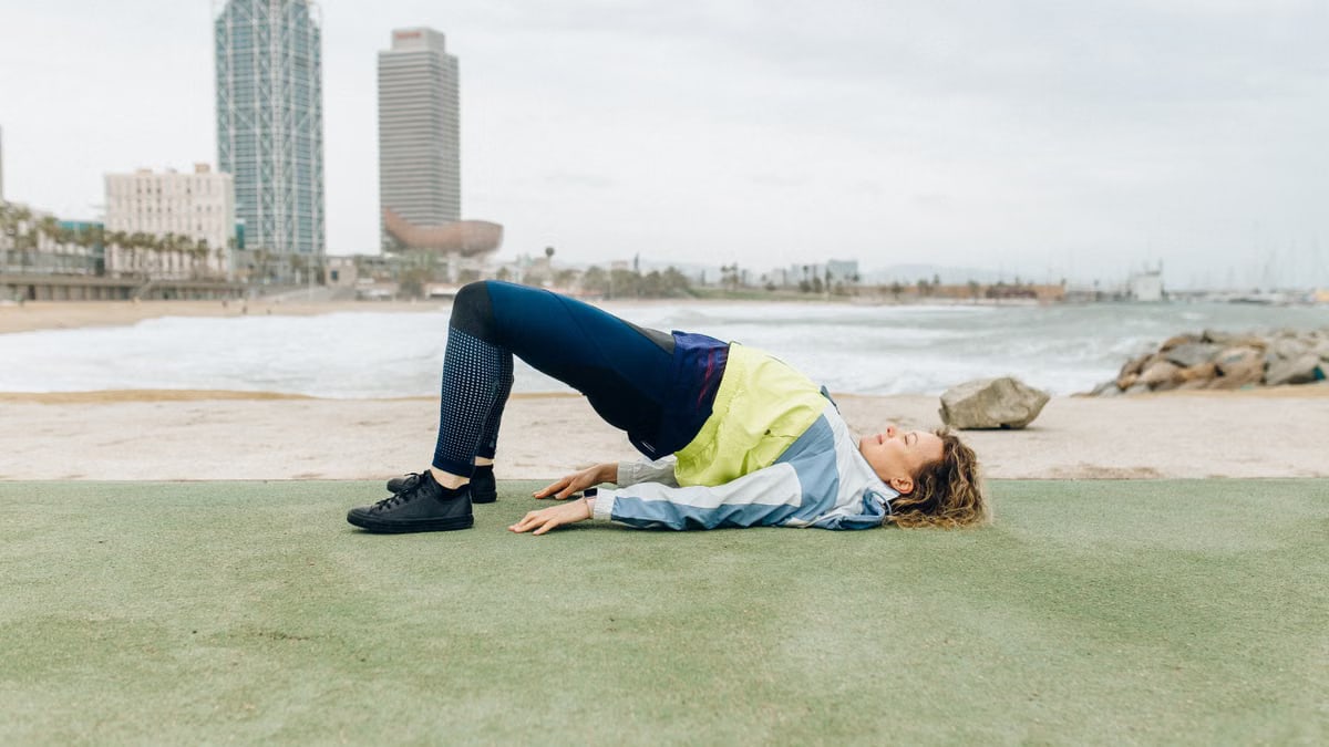A woman in activewear exercises near the beach with skyscrapers in the background, embodying a healthy lifestyle.